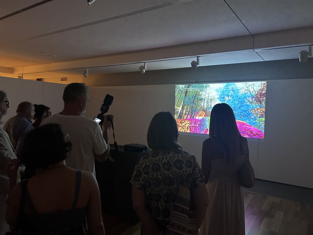 A crowd at the opening, one visitor photographing the projection on a camera