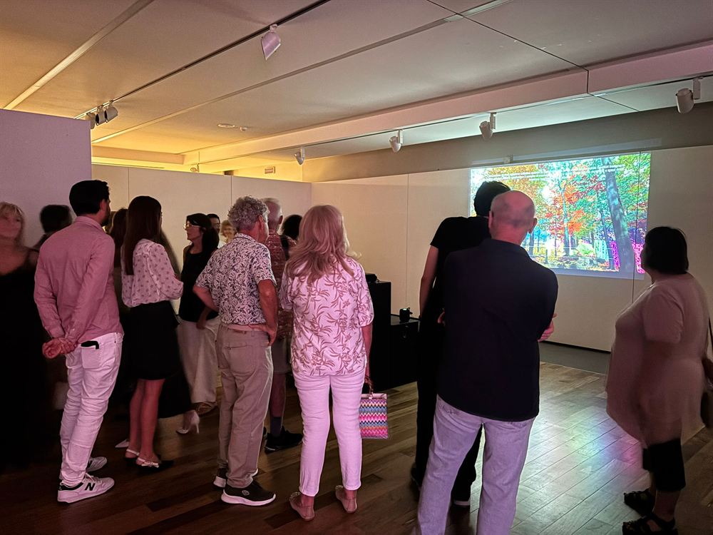 Opening night crowd filling the gallery, the projection glowing on the far wall