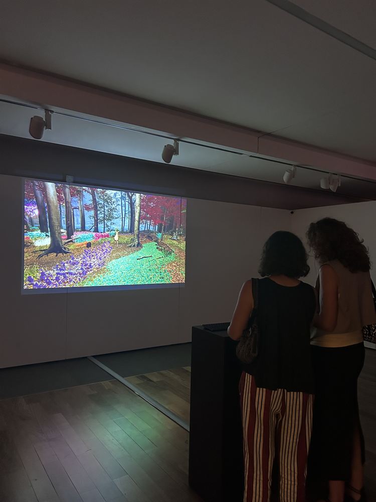 Two visitors standing at the plinth watching an intact, brightly coloured forest on the projection