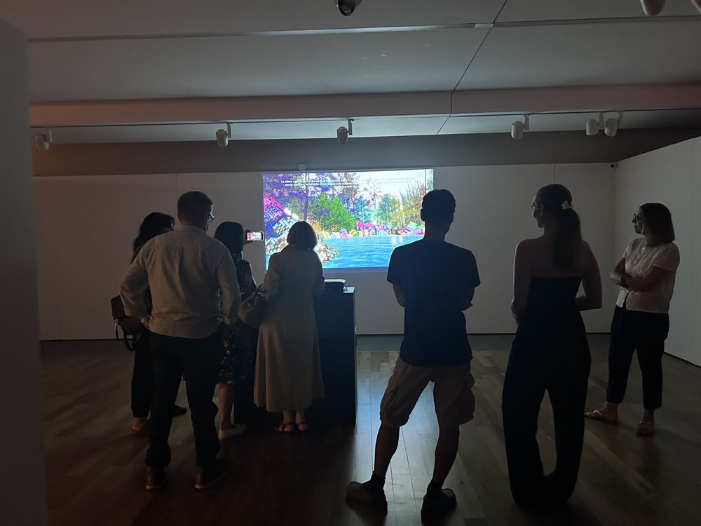 Six visitors silhouetted against the projection, the forest reflected in water on screen